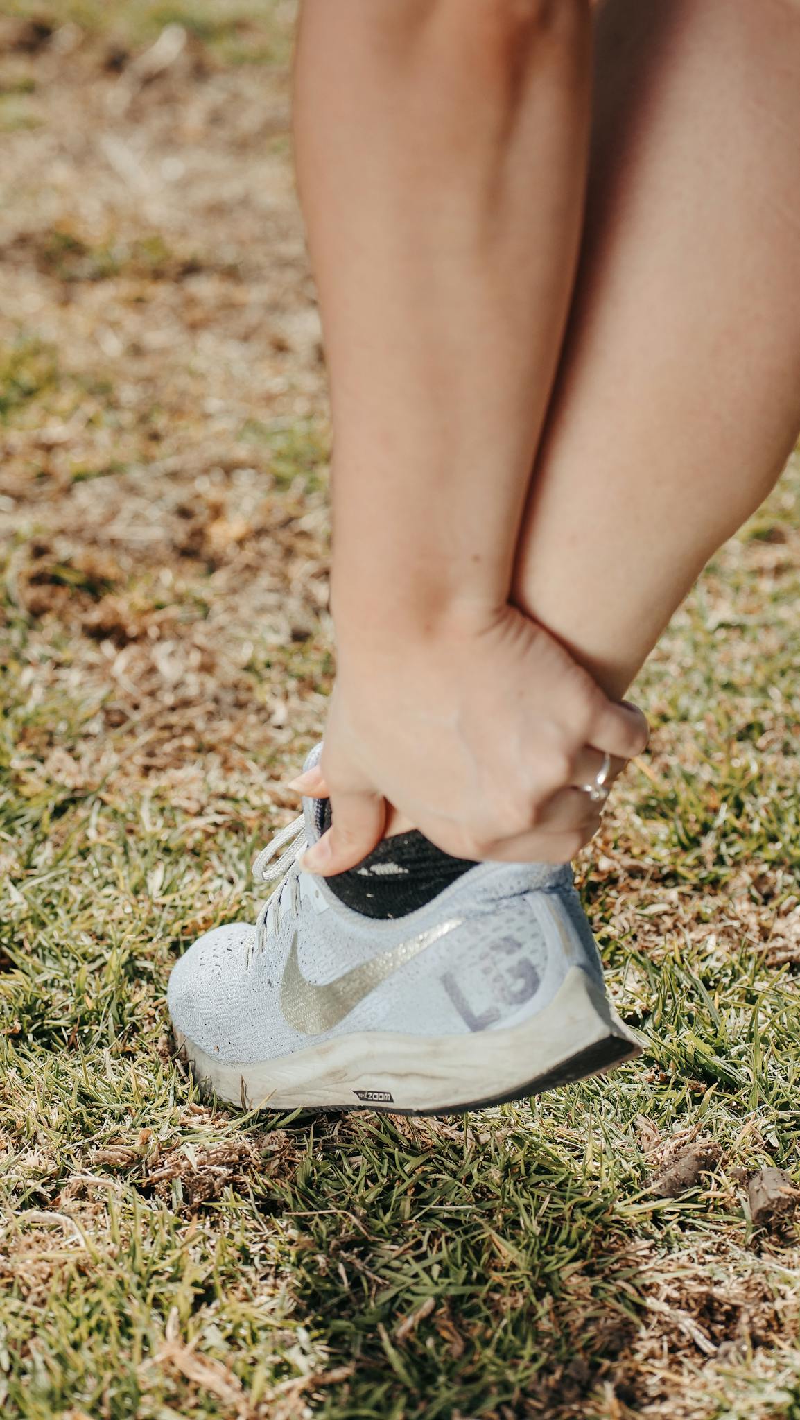 Close-up of a person holding their ankle in a sneaker, indicating pain or injury.